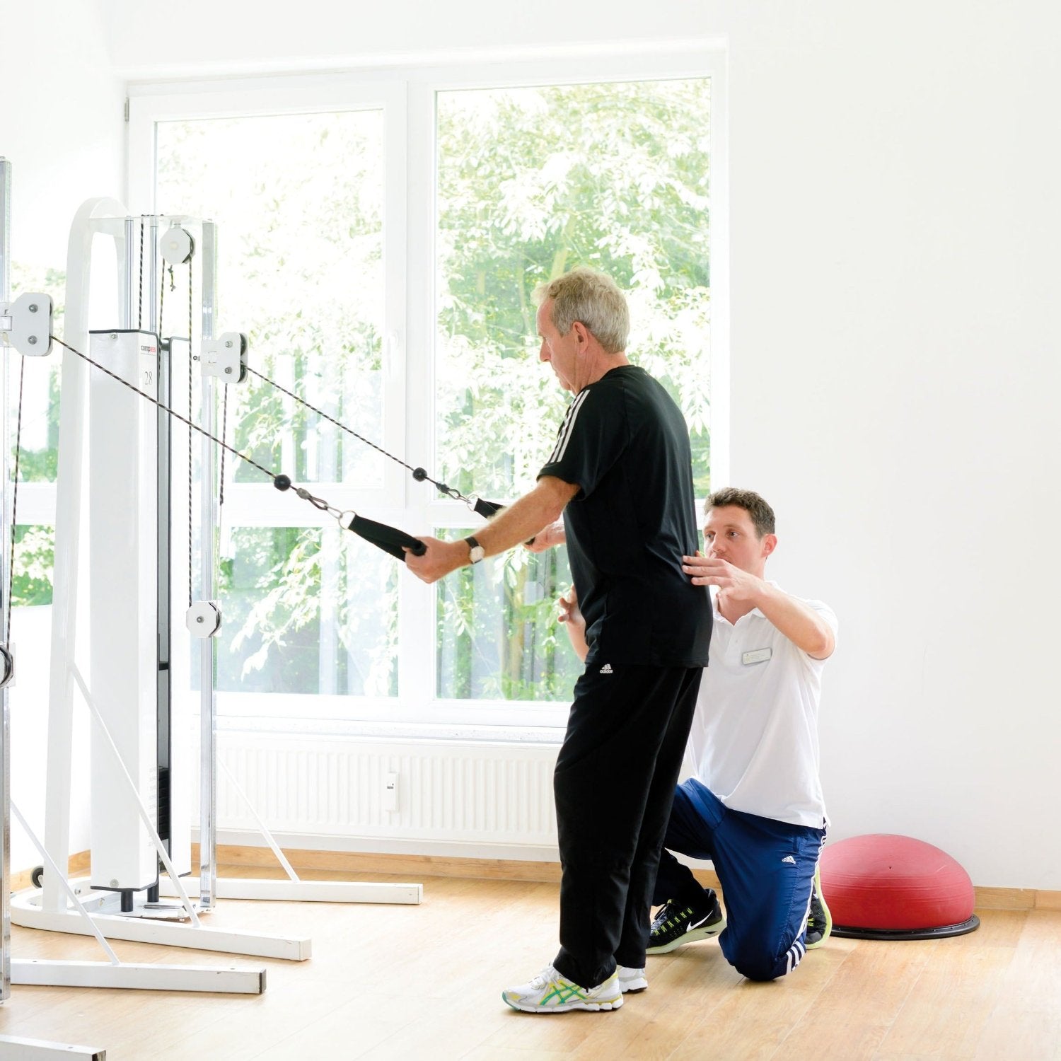 Medizinische Trainingstherapie: Physiotherapeut leitet Patient bei Kabelzugübung an während MTT-Training im ZAR Heilbronn.